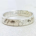 Silverfärgad ring med graverade blommotiv och text på insidan