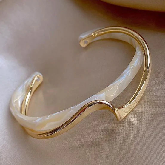 Öppet armband med guldfärgad finish och vågformad ljus detalj