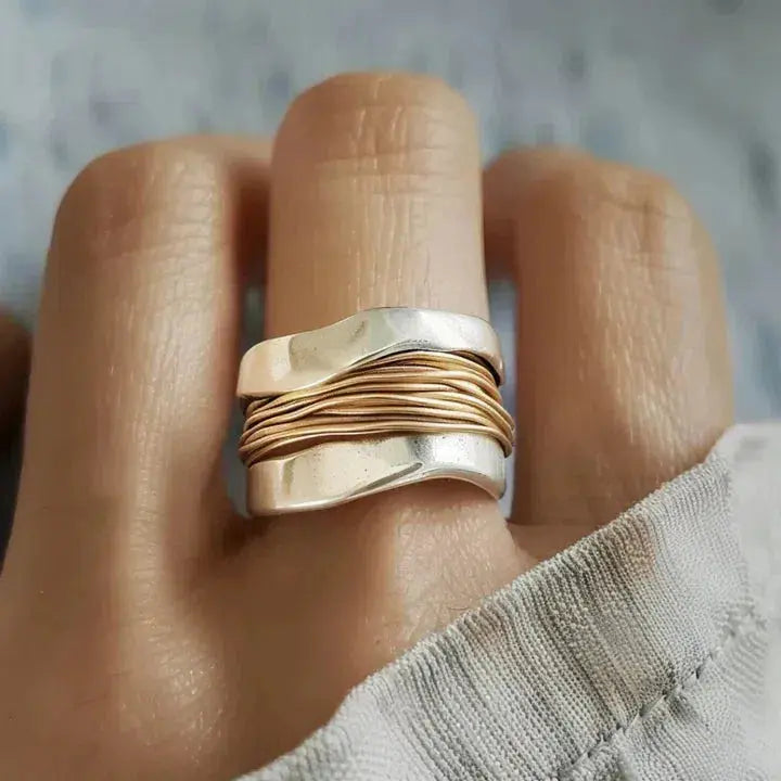 Bred guldfärgad ring med vågformade linjer och metallisk yta