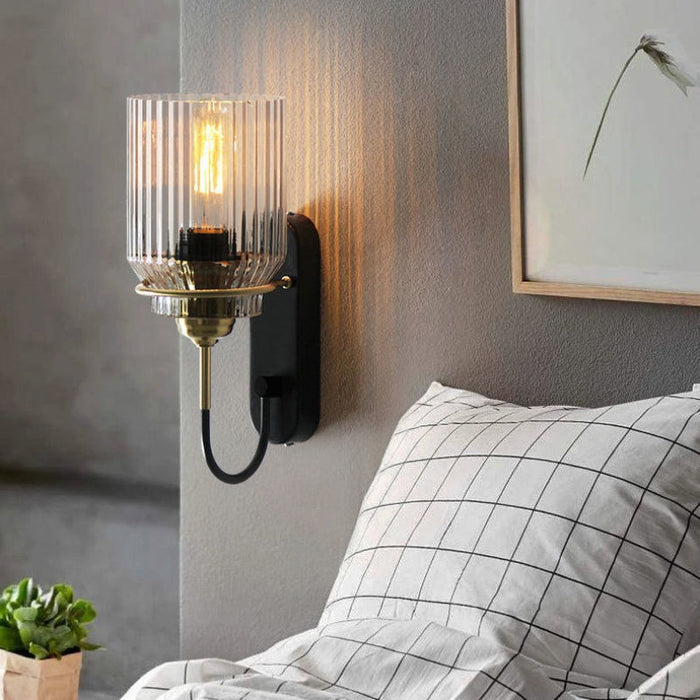 Vägglampa med räfflad klar glasskärm, svart fäste och guldfärgade detaljer
