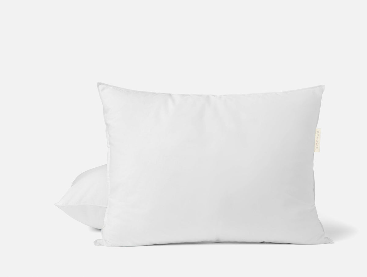 Vit dun- och fjäderkudde på en bäddad säng