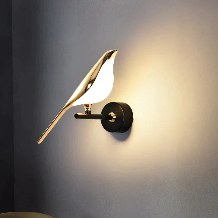 Guldfärgad vägglampa med fågeldesign och svart runt väggfäste