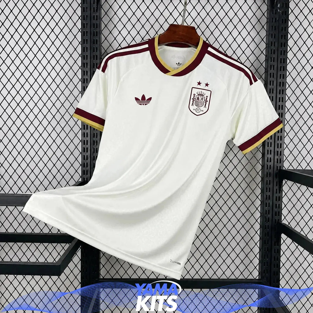 Vit fotbollströja med Spaniens emblem, två stjärnor och vinröda samt gula detaljer