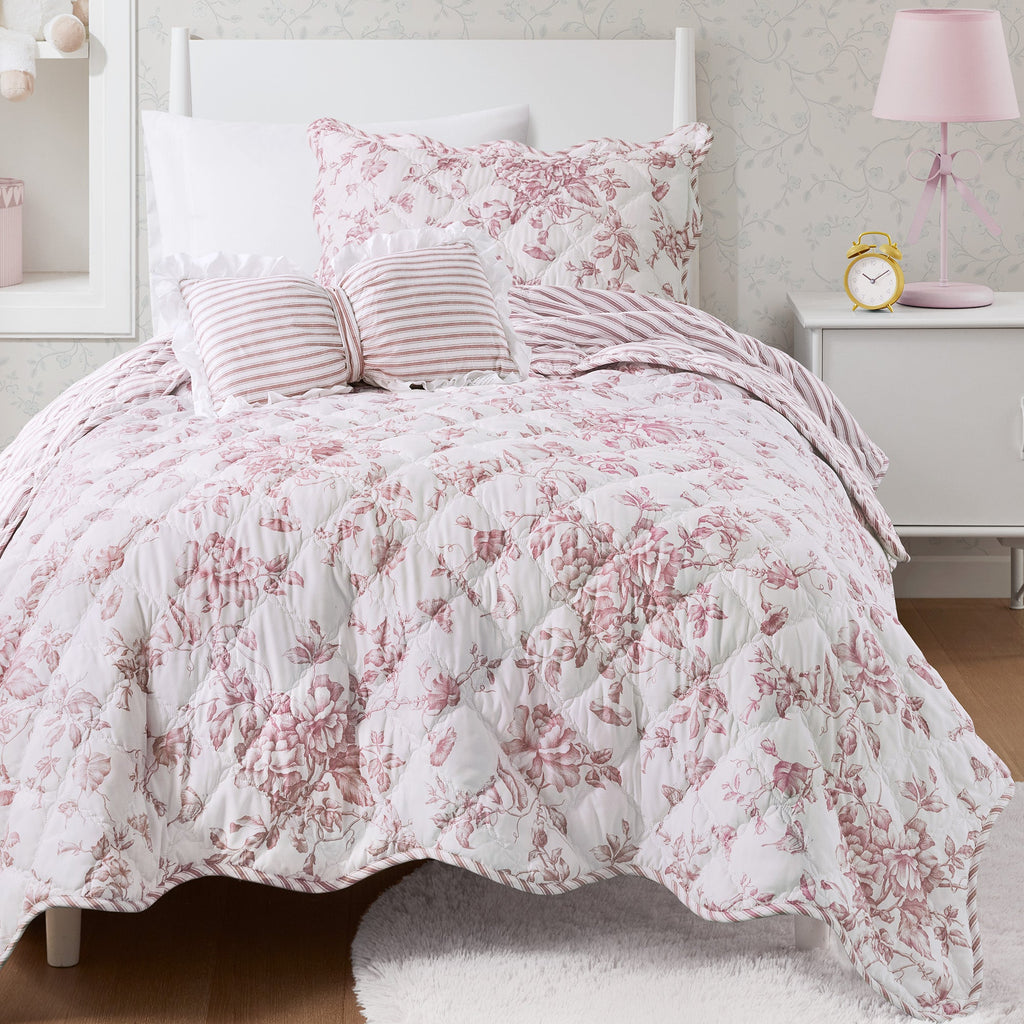 Quiltset med blommigt mönster, volangkant och dekorativ kudde på bäddad säng