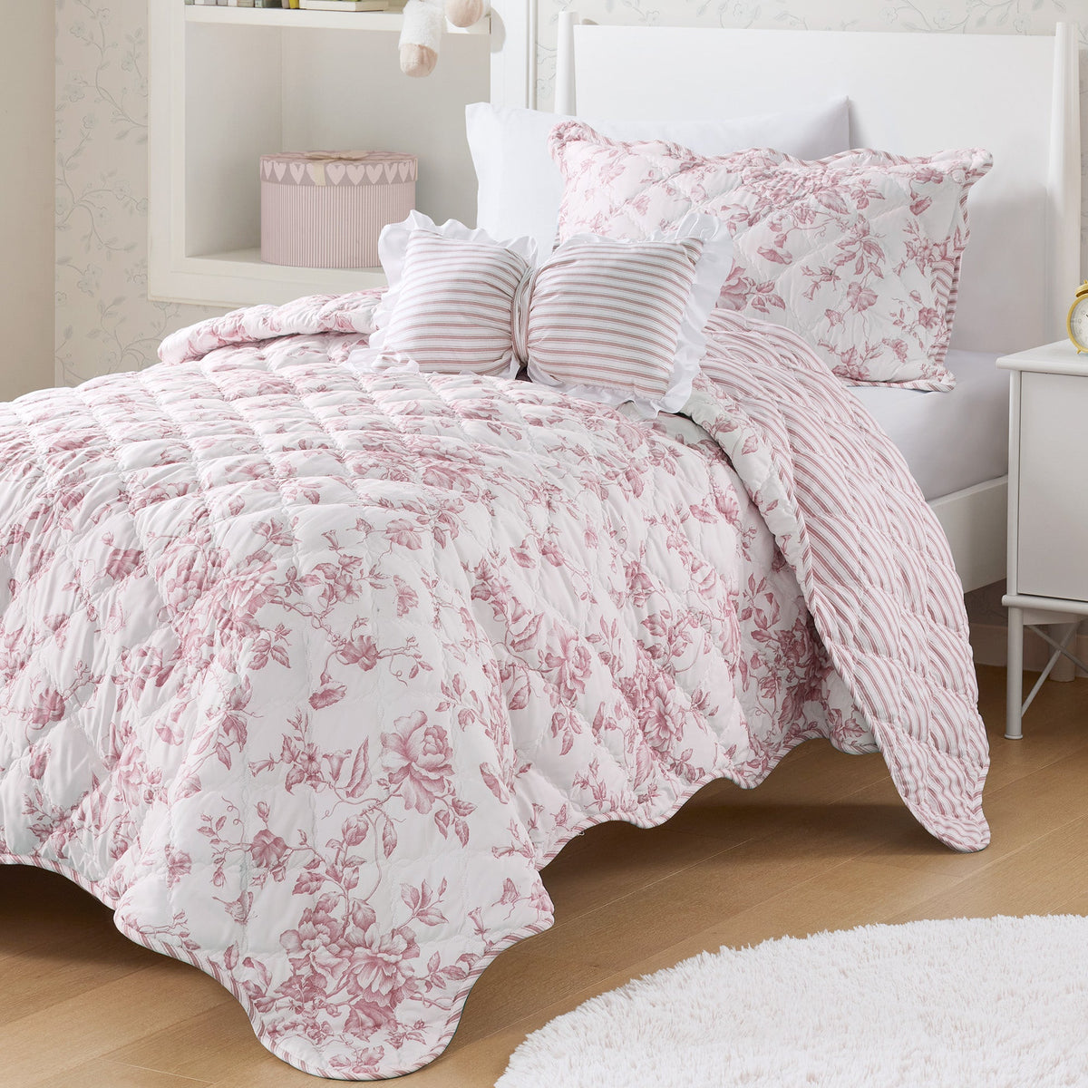 Quiltset med blommigt mönster, volangkant och dekorativ kudde på bäddad säng