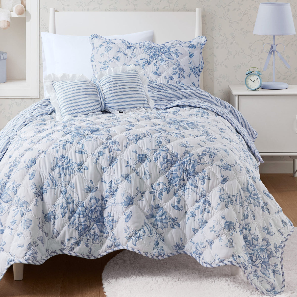 Quiltset med blommigt mönster, volangkant och dekorativ kudde på bäddad säng