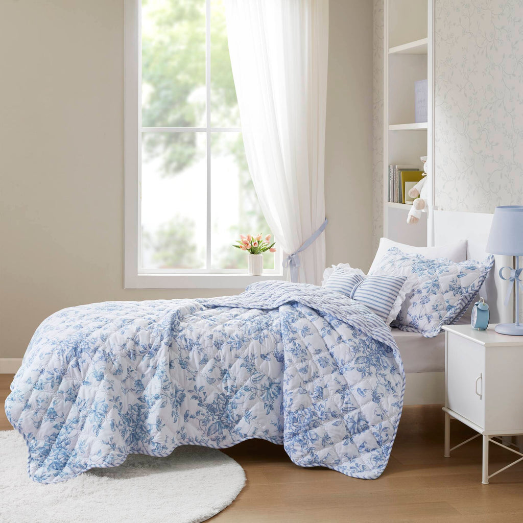 Quiltset med blommigt mönster, volangkant och dekorativ kudde på bäddad säng