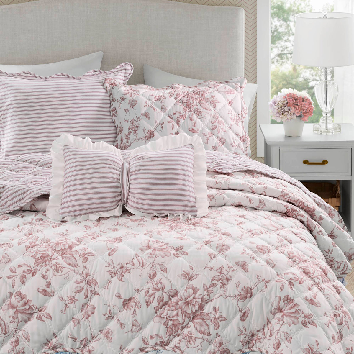 Quiltset med blommigt mönster, volangkant och dekorativ kudde på bäddad säng