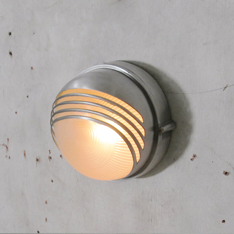 Grå vägglampa med räfflat glas monterad vid en ytterdörr
