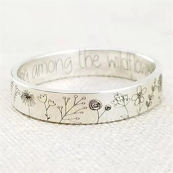 Silverfärgad ring med graverade blommotiv och text på insidan