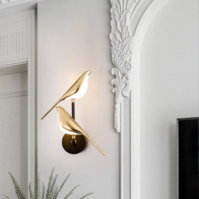 Guldfärgad vägglampa med fågeldesign och svart runt väggfäste
