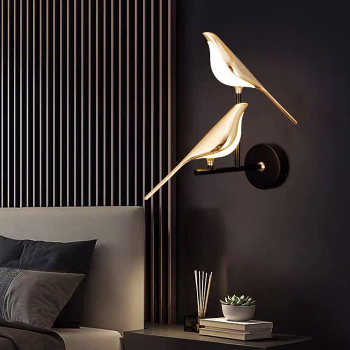 Guldfärgad vägglampa med fågeldesign och svart runt väggfäste